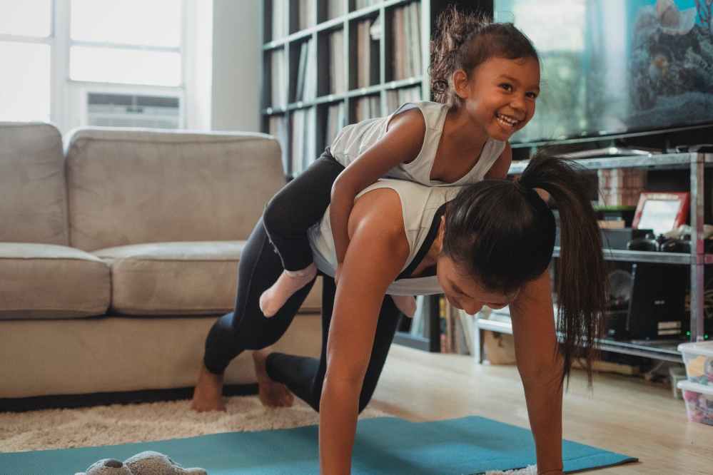 young asian woman piggybacking smiling daughter while exercising at home