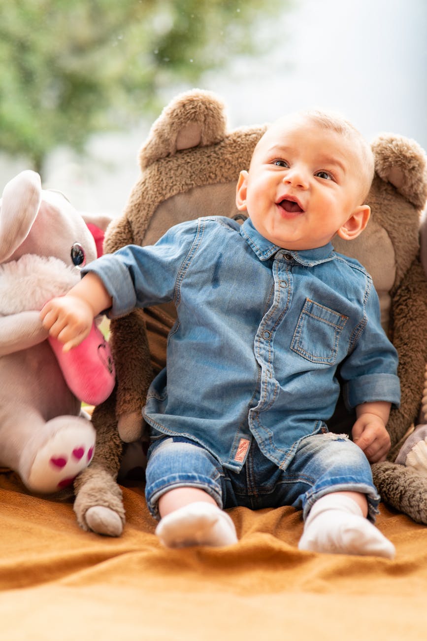 baby in blue denim button up jacket and blue denim jeans sitting on brown bear plush toy